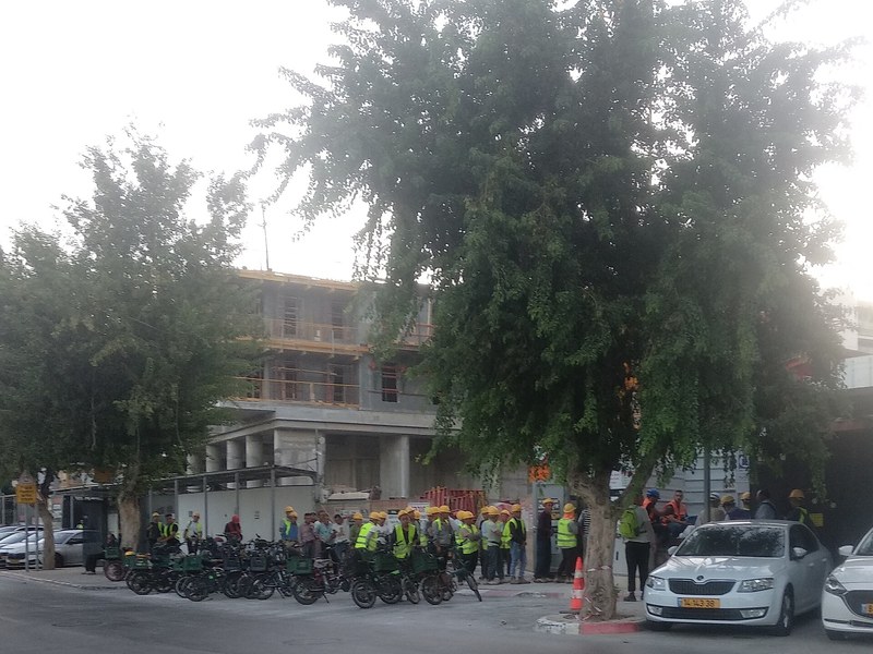 עובדי בניין סינים מתאספים בתחילת יום עבודה באתר בנייה בהרצליה