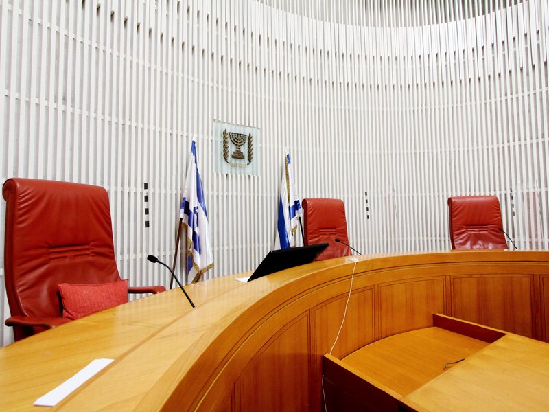 אולם דיונים ריק בבית המשפט העליון בישראל ובו שלושה כיסאות שופטים
