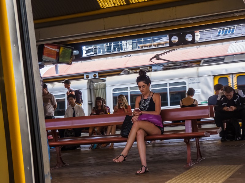 נוסעים ממתינים ברציף רכבת ומעיינים בטלפונים חכמים