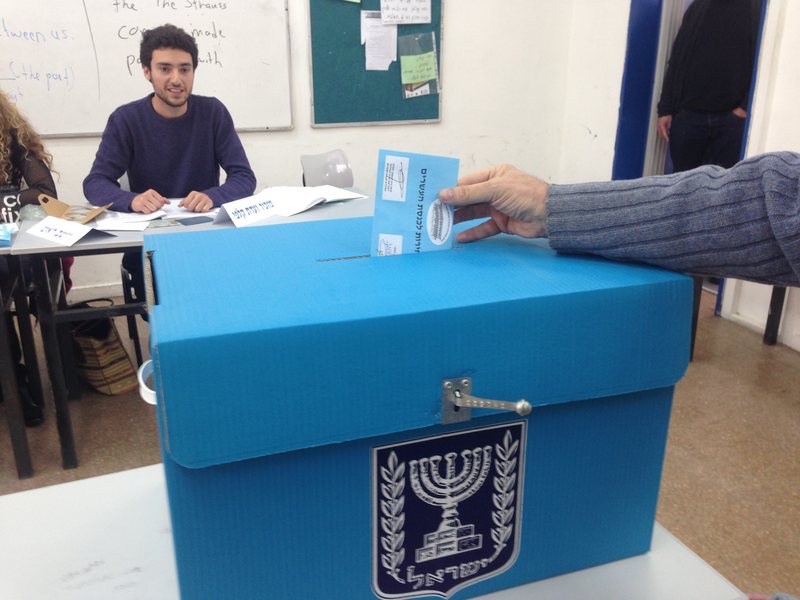 ידו של מצביע מכניסה מעטפת הצבעה לקלפי כחולה בבחירות לכנסת בישראל