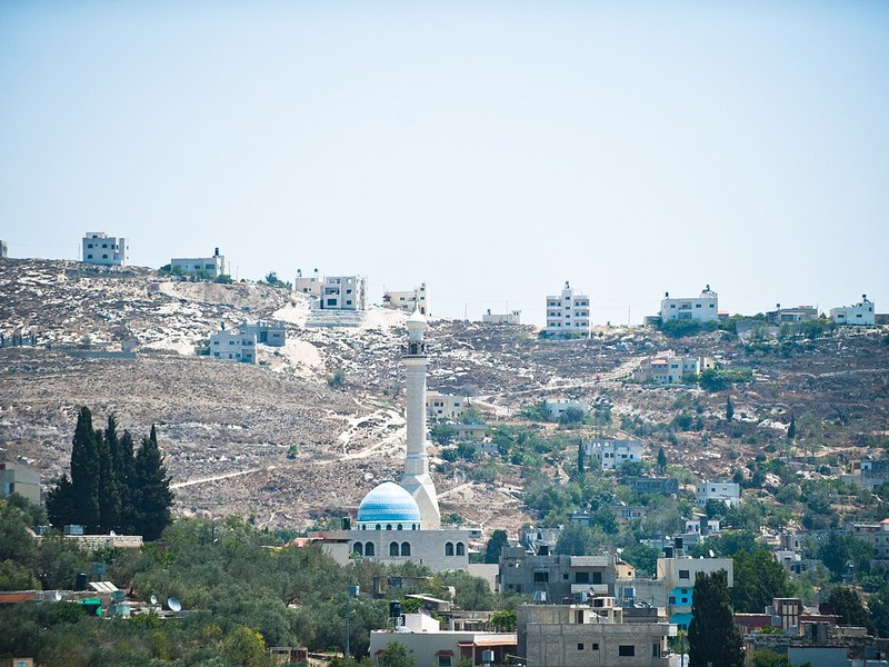 מסגד ובתי יישוב פלסטיני בעמק, ומעליהם בתי התנחלות על גבעה בגדה המערבית